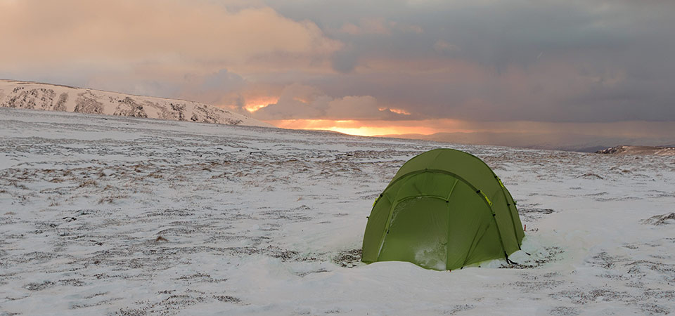 Quadratic tent pitched on snow with sunset and clouds behind